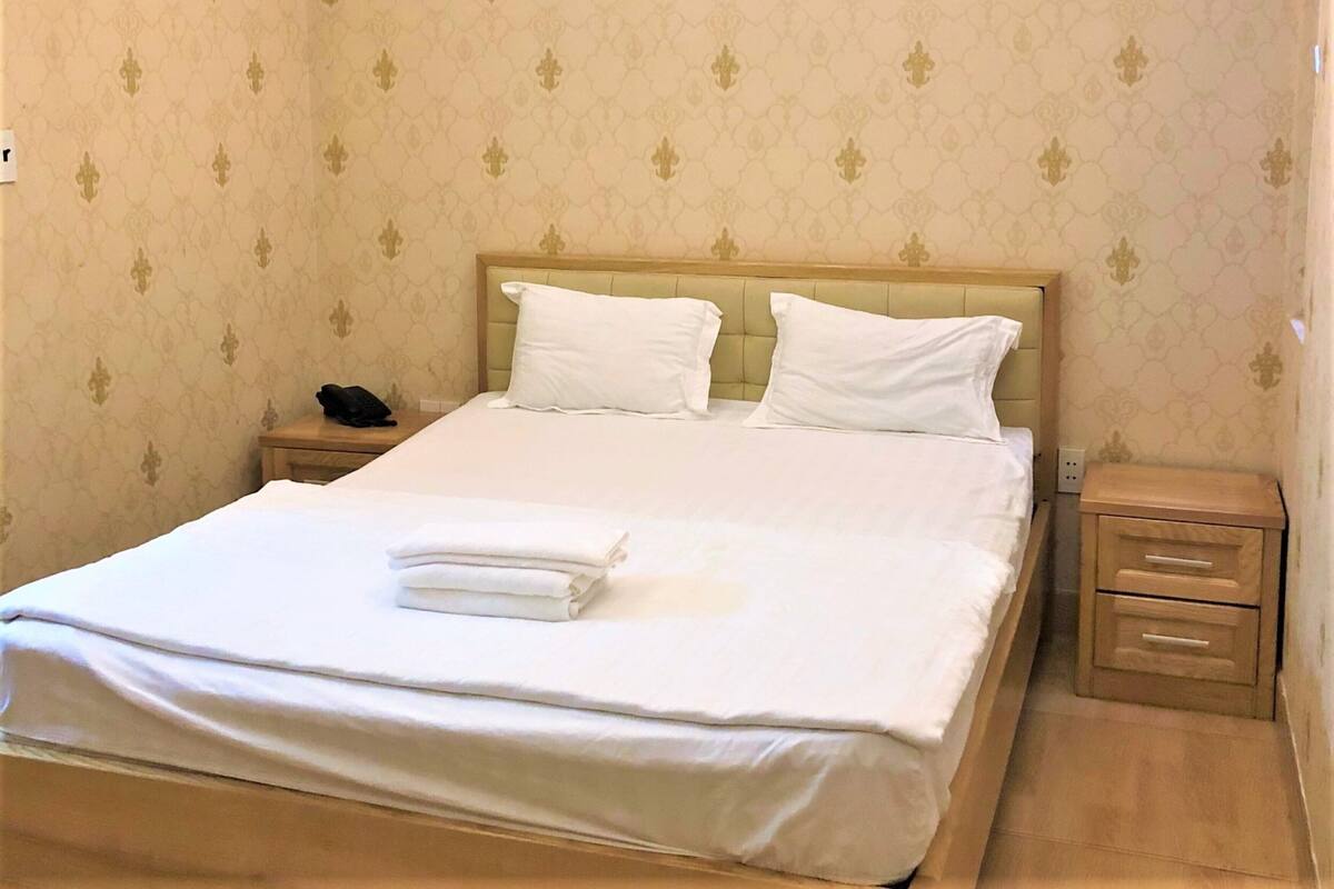 Ein ordentlich bezogenes Bett mit weißen Leinen und Kissen, ein Nachttischtelefon und ein kleiner Nachttisch mit Schubladen.