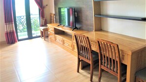 Ein modernes Wohnzimmer mit einem Holzespeisetisch, zwei Holzstühlen, einem Fernseher auf einem Standfuß und einem Balkon mit roten Vorhängen.