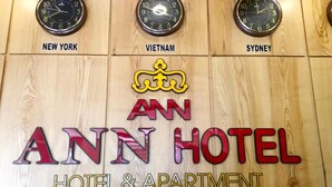 Eine Holzwand mit Uhren, auf denen 'New York', 'Vietnam' und 'Sydney' stehen, sowie der Schriftzug 'AN ANN HOTEL HOTEL & APARTMENT' und ein Wappensymbol darüber.