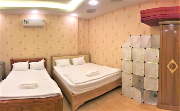 A hotel room with two beds, a wardrobe, and a ceiling fan.