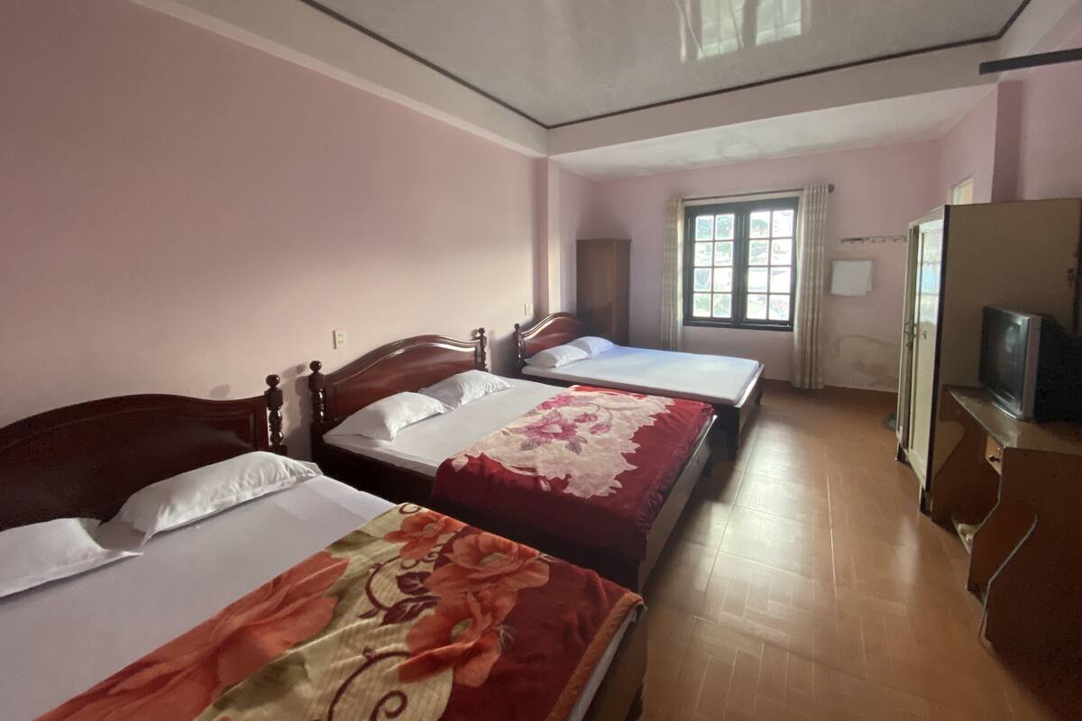 A room with two beds, a window with curtains, and a television on a wooden cabinet.