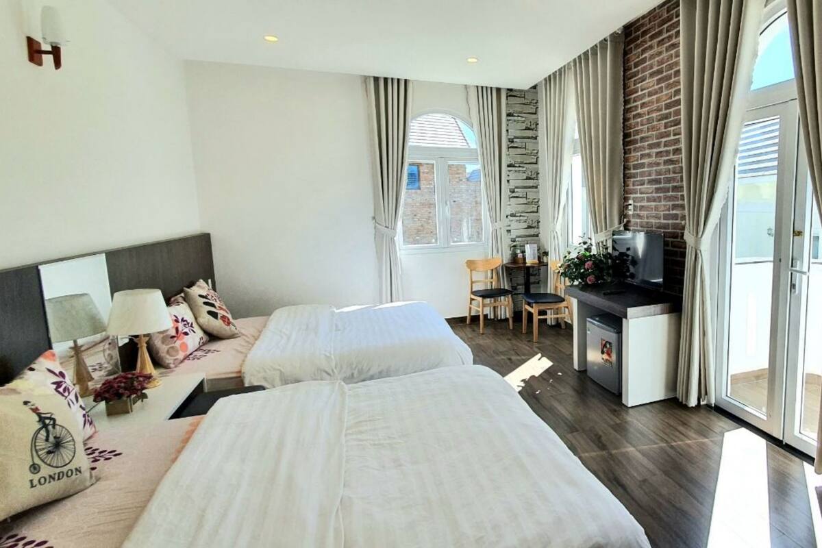 A hotel room with two beds, a desk, a TV, and a view of the outdoors.