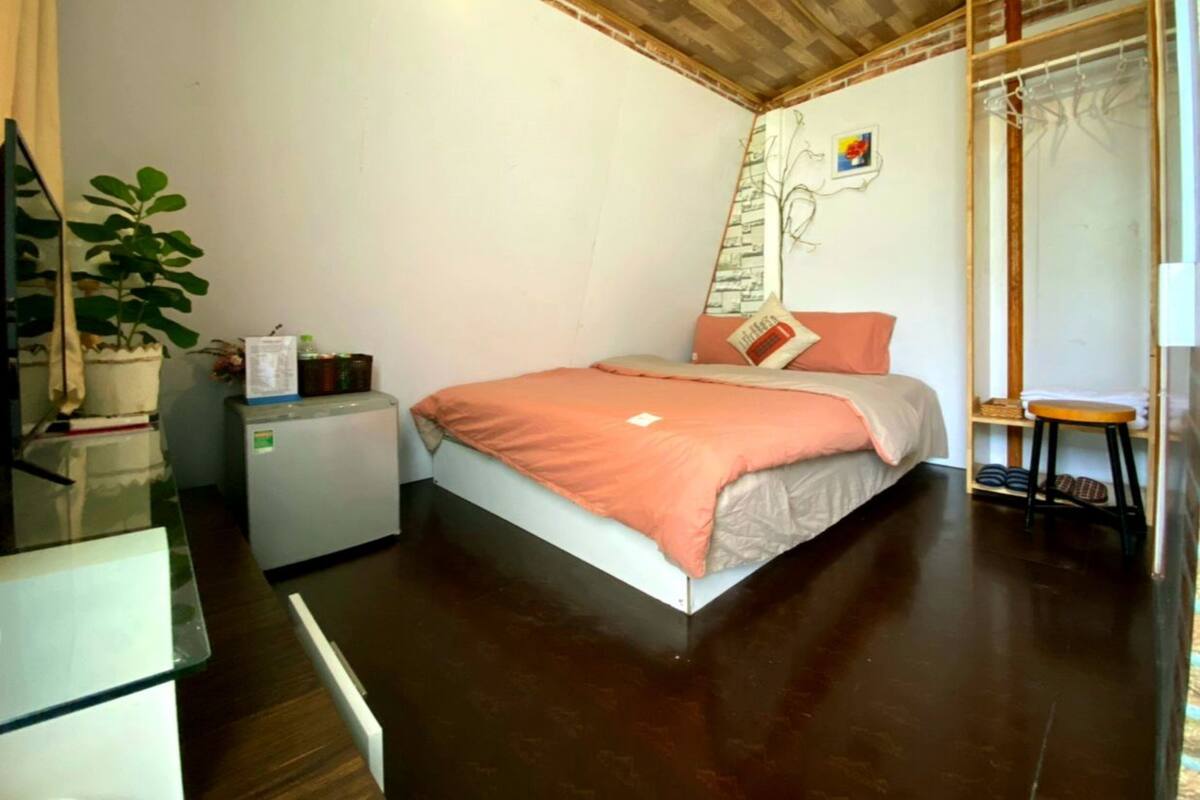 A small, cozy bedroom with a single bed, a desk, a chair, and a potted plant.