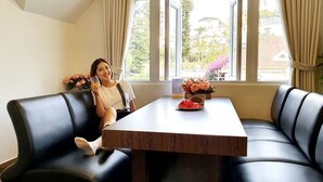 A person sitting on a black leather couch at a wooden table with a vase of flowers and a plate of watermelon slices. - Pho Hoa Boutique Villa (Cam Ly - Da Lat)