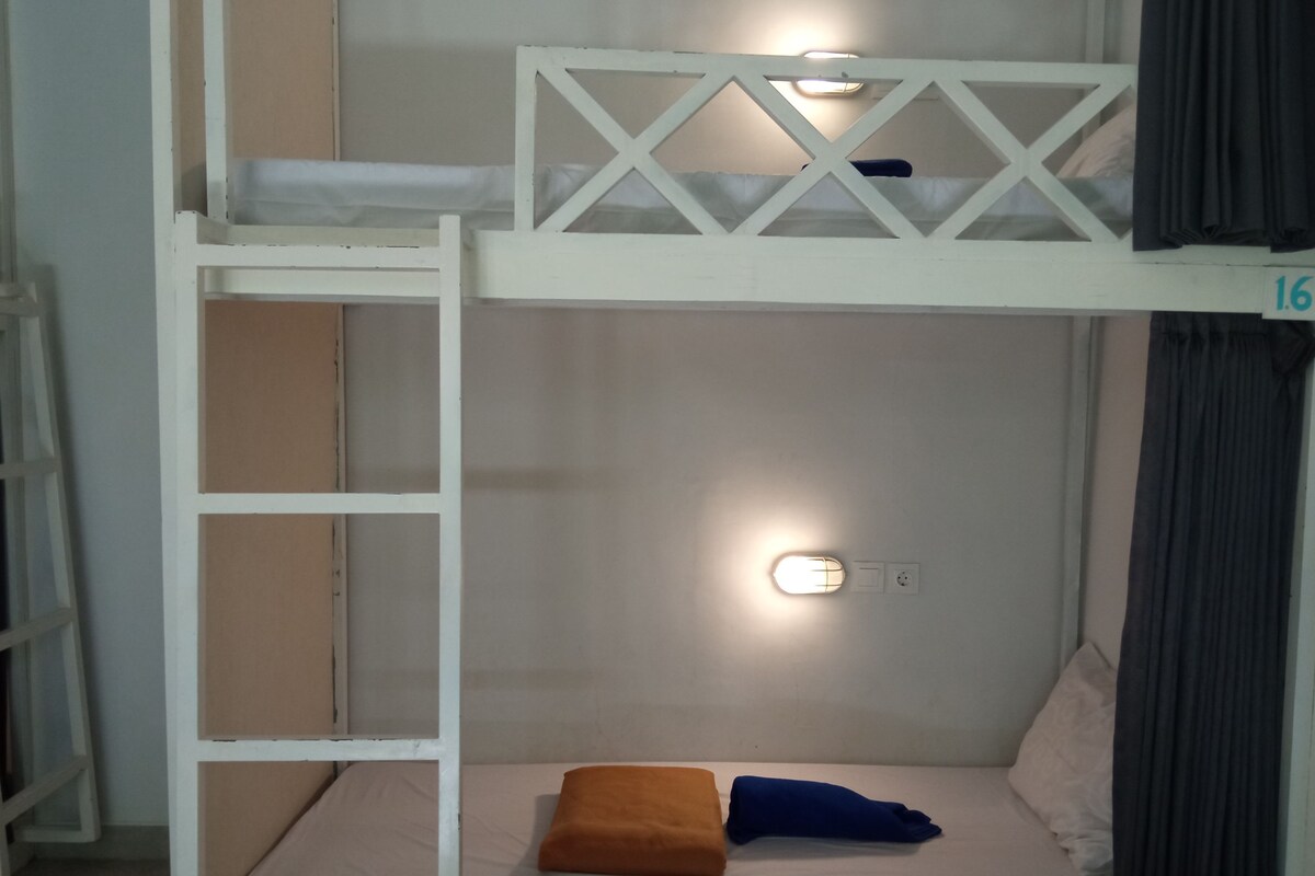 Una cama litera con escalera, una luz instalada en la pared y una cama individual con dos almohadas.