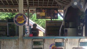 A snack point with a menu board, a water dispenser, and a person behind the counter. - Ms Snack Point Bed & Breakfast (Canggu)