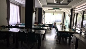 A spacious dining area with multiple tables and chairs, large windows with curtains, and a chandelier. - Grand Balqis Akasia Hotel (Surabaya)