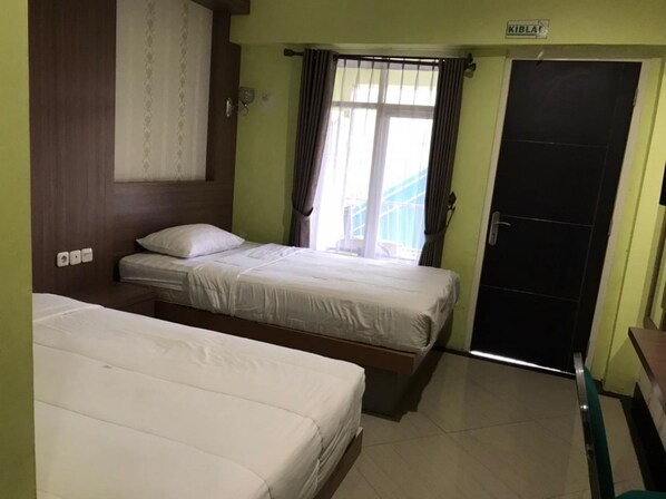 Une chambre d’hôtel avec deux lits, une fenêtre avec des rideaux, une porte et une pancarte au-dessus de la porte.