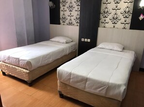 Deux lits simples avec du linge de lit blanc, dans une chambre dont un mur est décoré d’un motif et qui est équipée d’un luminaire.