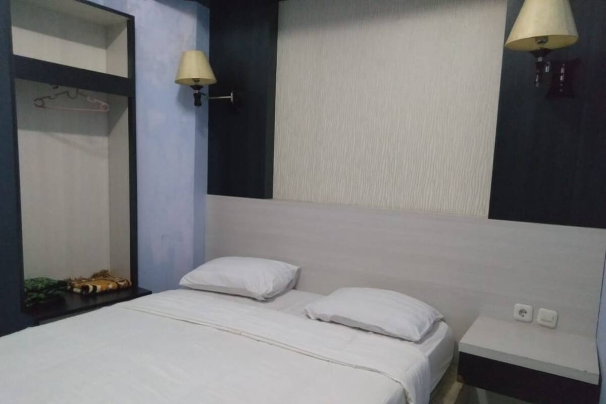 Ein Hotelzimmer mit einem Bett, zwei Kissen, einem Nachttisch, einer Lampe und einem Spiegel.