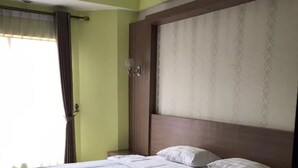 A neatly made bed in a room with a green wall, a wooden headboard, and a window with curtains. - Grand Balqis Akasia Hotel (Surabaya)