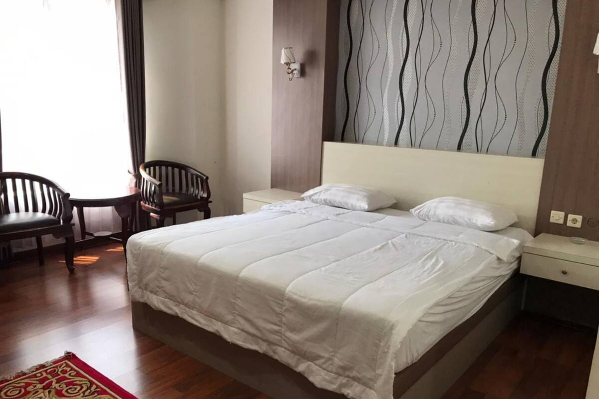 Ein Schlafzimmer mit einem großen Bett, einem Holzstuhl, einem kleinen Tisch und einer Wand mit Muster.