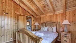 Een slaapkamer in een houten blokhut met een bed, nachtkastjes en een houten hoofdbord.