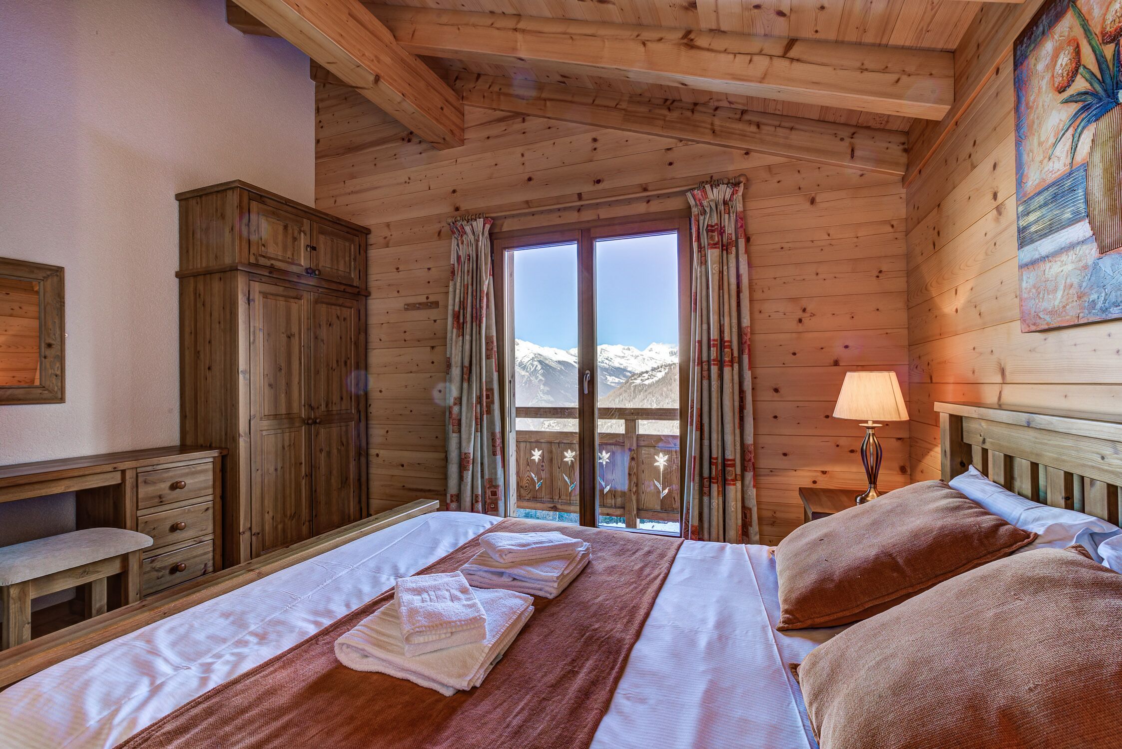 Une chambre dans une cabane en bois, avec un lit, une armoire en bois, un bureau et une fenêtre donnant sur des montagnes enneigées.