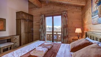 Une chambre dans une cabane en bois, avec un lit, une armoire en bois, un bureau et une fenêtre donnant sur des montagnes enneigées.