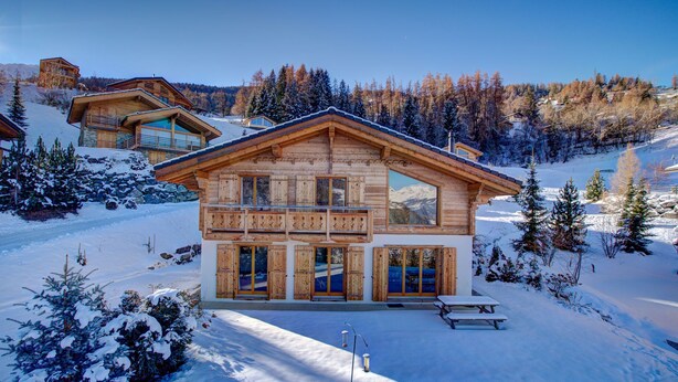 A wooden chalet with a balcony, a wooden deck, and a snow-covered landscape.
