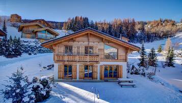 Un chalet en bois doté d’un balcon, d’une terrasse en bois et surplombant un paysage enneigé.