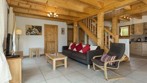 A wooden interior with a sofa, a chair, a small table, a staircase, and a kitchen area.