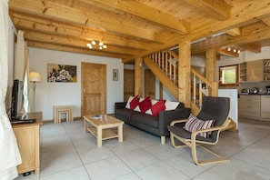 Ein Holzinterieur mit einer Couch, einem Sessel, einem kleinen Tisch, einer Treppe und einer Küchenzeile.