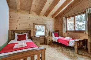 Ein Schlafzimmer einer Holzhütte mit zwei Betten, Holz-Kopfteilen und einem großen Fenster mit Blick auf Bäume.