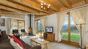 A living room with a wooden ceiling, a television, a sofa, a coffee table, and a view of mountains through large windows.