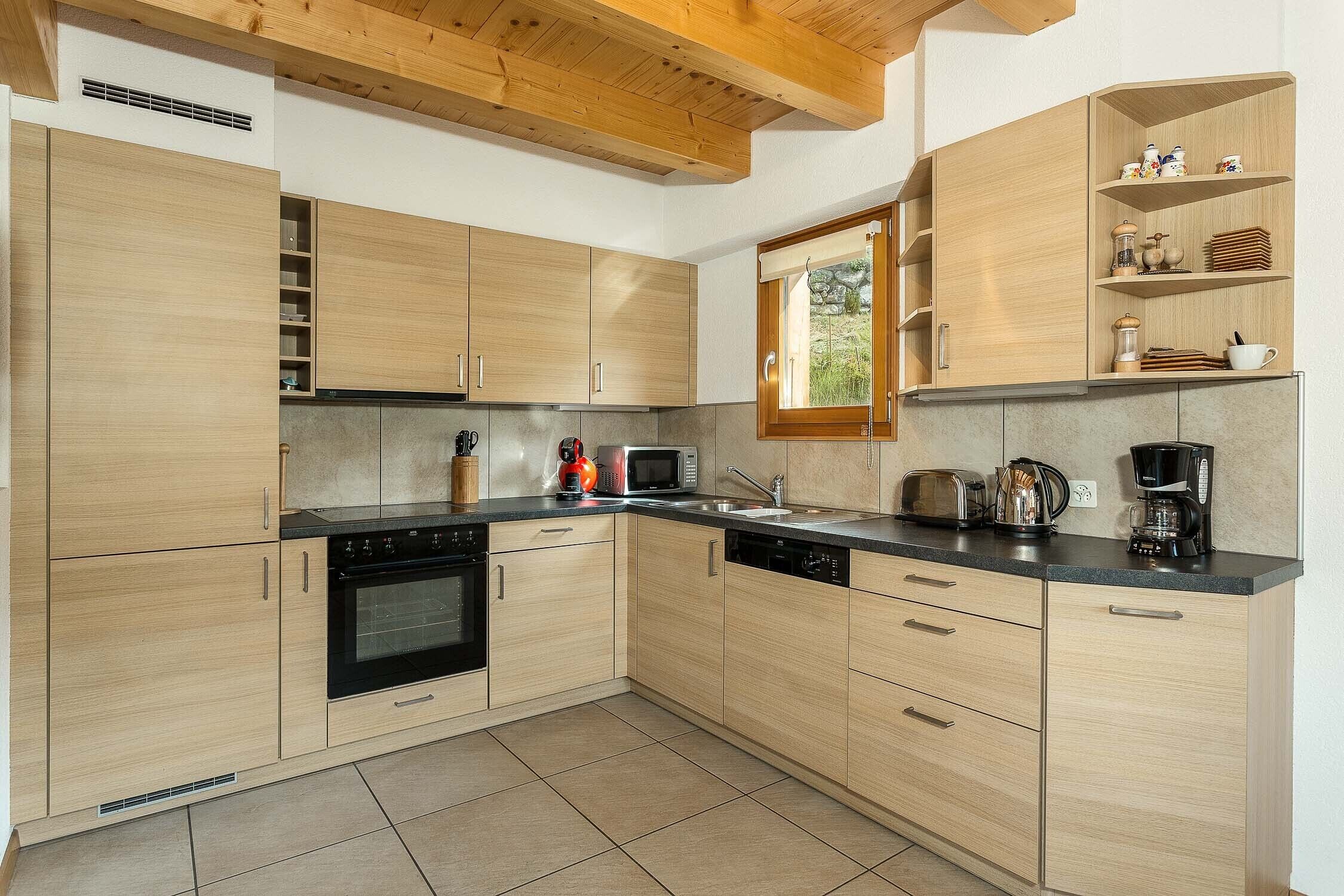 A modern kitchen with light wood cabinets, a black oven, and a microwave. There is a window above the sink, and a shelf with kitchen items.