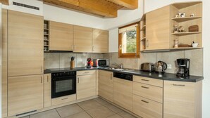 A modern kitchen with light wood cabinets, a black oven, and a microwave. There is a window above the sink, and a shelf with kitchen items.