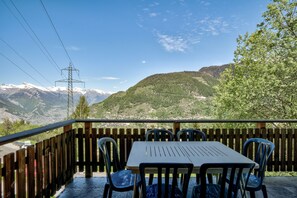 A terrace with a table and chairs, overlooking a mountainous landscape with a power line structure.