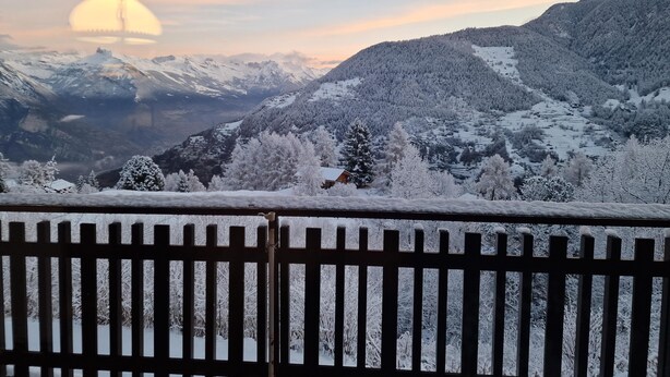 Un paysage de montagne enneigé, avec un ciel dégagé et un soleil lointain.