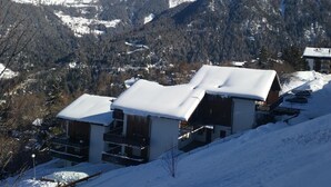 Une station de montagne enneigée, avec des bâtiments de style chalet, une piste de ski et une vue dégagée sur les montagnes environnantes.