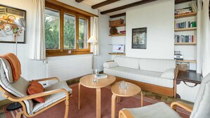 Une pièce confortable avec un canapé, deux fauteuils, une petite table, une bibliothèque et une fenêtre avec des rideaux.