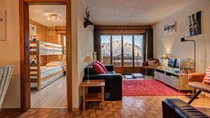 A cozy room with a bunk bed, a sofa, a desk, and a chair. There is a large window with a mountain view. - Appartement Bellevue 207 - La Tzoumaz, 4 Vallees (La Tzoumaz)