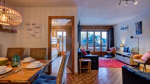 A cozy room with a dining table set for four, a sofa, a small desk, and a view of mountains through the window. - Appartement Bellevue 207 - La Tzoumaz, 4 Vallees (La Tzoumaz)