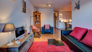A living room with a TV, sofa, and armchair, a wooden cabinet, and a red carpet. - Appartement Bellevue 207 - La Tzoumaz, 4 Vallees (La Tzoumaz)