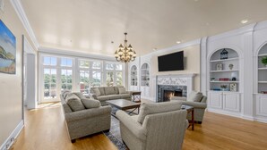 A spacious living room with a fireplace, large windows, and a chandelier. - LakeViews, Indoor/Outdoor Pools, HotTub & Fire Pit (Branson)