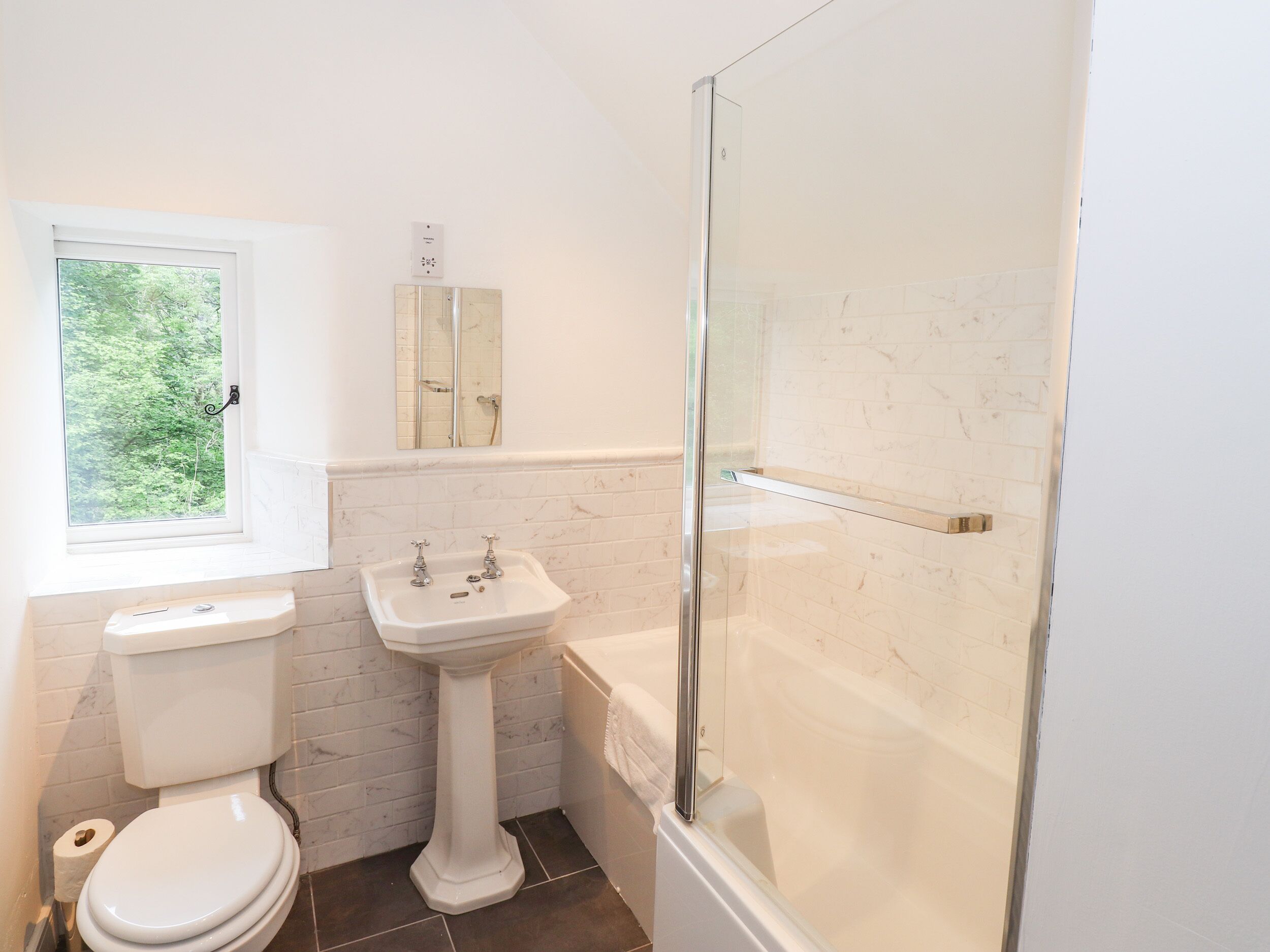 A bathroom with a toilet, pedestal sink, and a glass-enclosed shower.