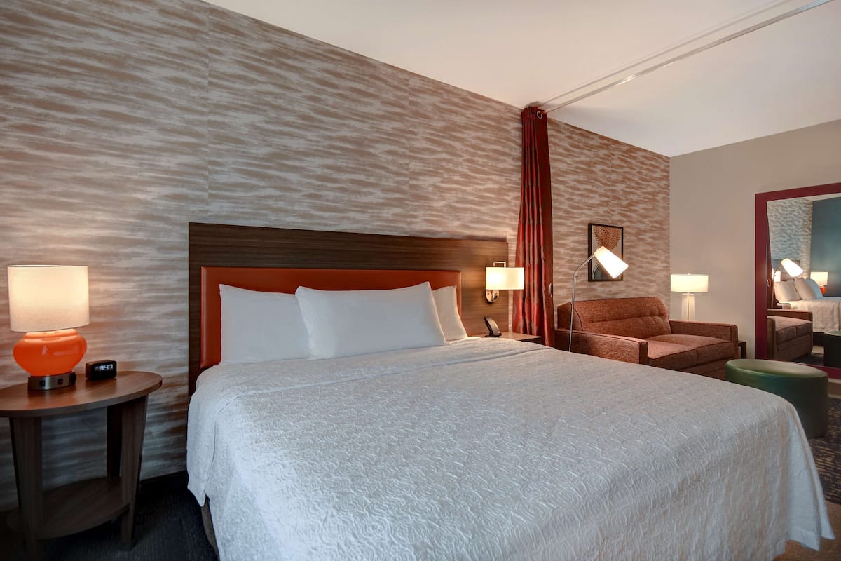 A hotel room with a large bed, two bedside tables with lamps, a chair, and a small ottoman.
