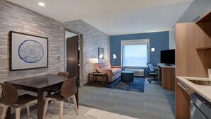 Ein modernes Hotelzimmer mit Essbereich, einer Couch, einem Fernseher und einer Küchenzeile.