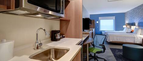 A compact hotel room with a kitchenette, a bed, a desk, and a chair.