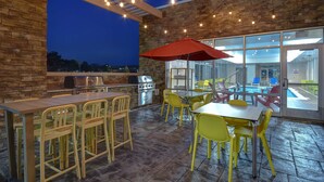 Eine Außenpatio-Terrasse mit einem Grill, gelbgrünen Stühlen und einem roten Sonnenschirm.