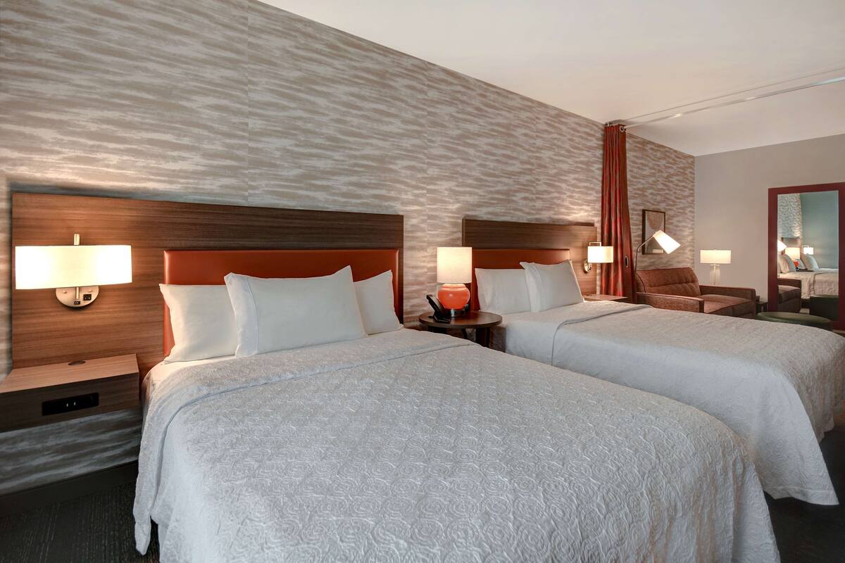 A hotel room with two beds, nightstands, lamps, a mirror, and a textured wall.