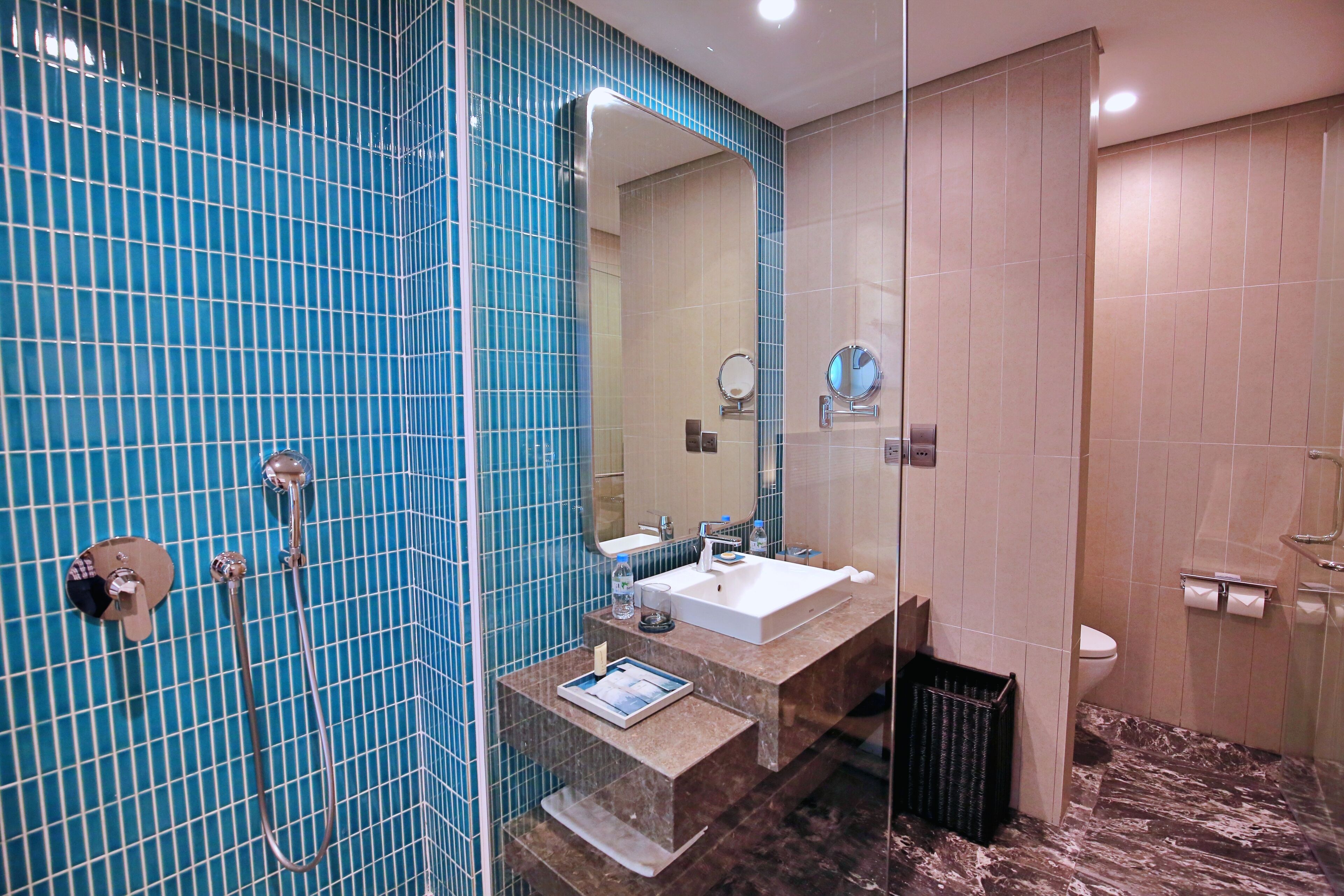 A bathroom with a blue tiled wall, a sink, a mirror, and a shower area.