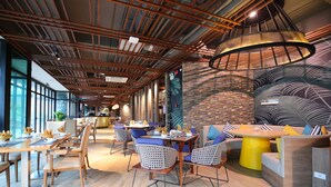 A modern restaurant with wooden tables and chairs, large windows, and a unique ceiling design. - FLC City Hotel Beach Quy Nhon (Quy Nhon Nam)