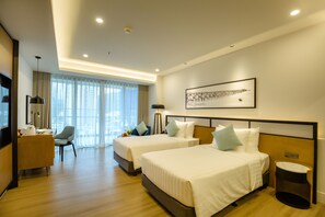 A hotel room with two beds, a desk, a chair, a bedside table, and a large window with curtains. - FLC City Hotel Beach Quy Nhon (Quy Nhon)