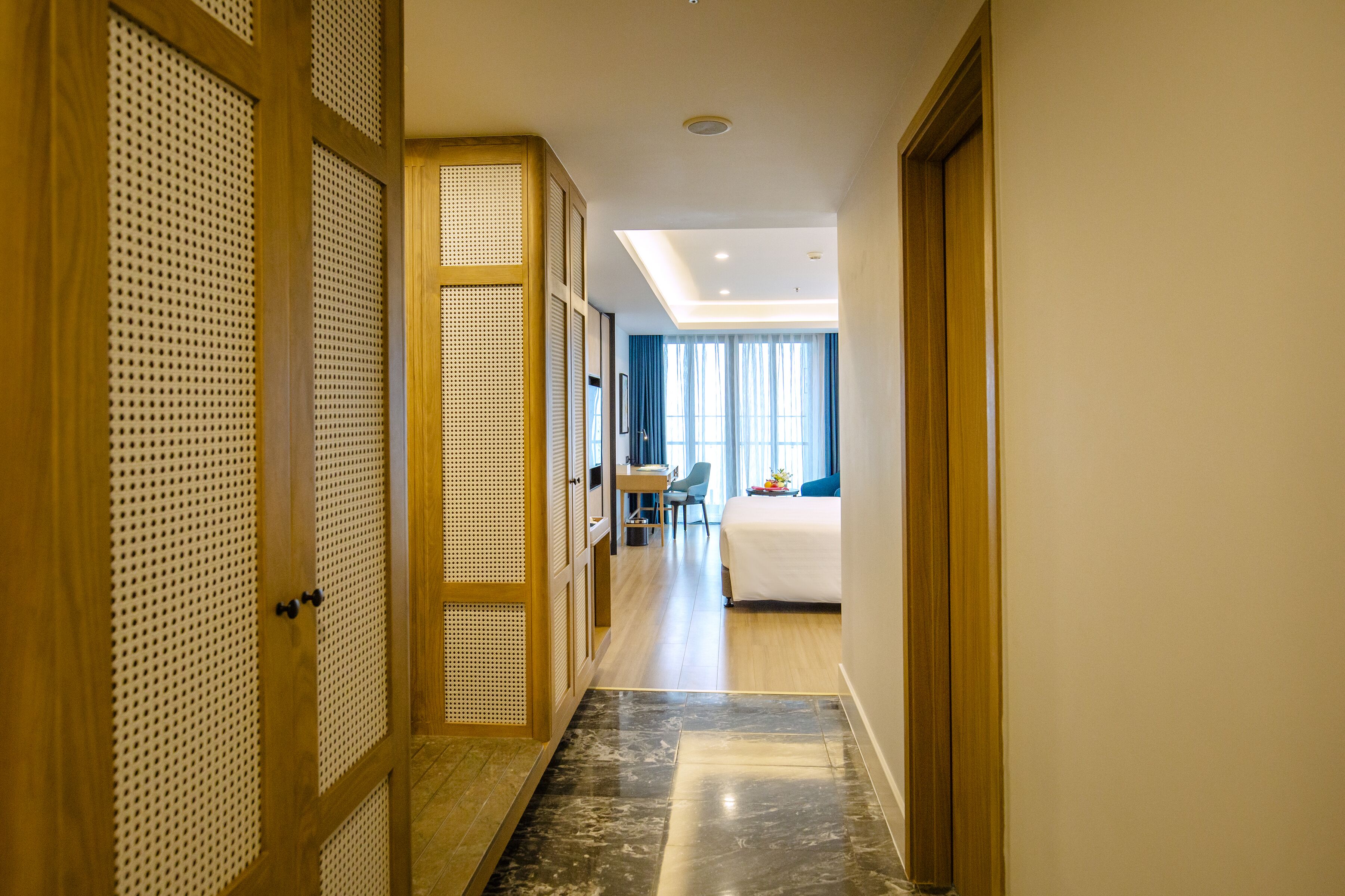 Ein Hotelkorridor mit einer Holztür, einem Schreibtisch, einem Bett und Blick ins Zimmer.