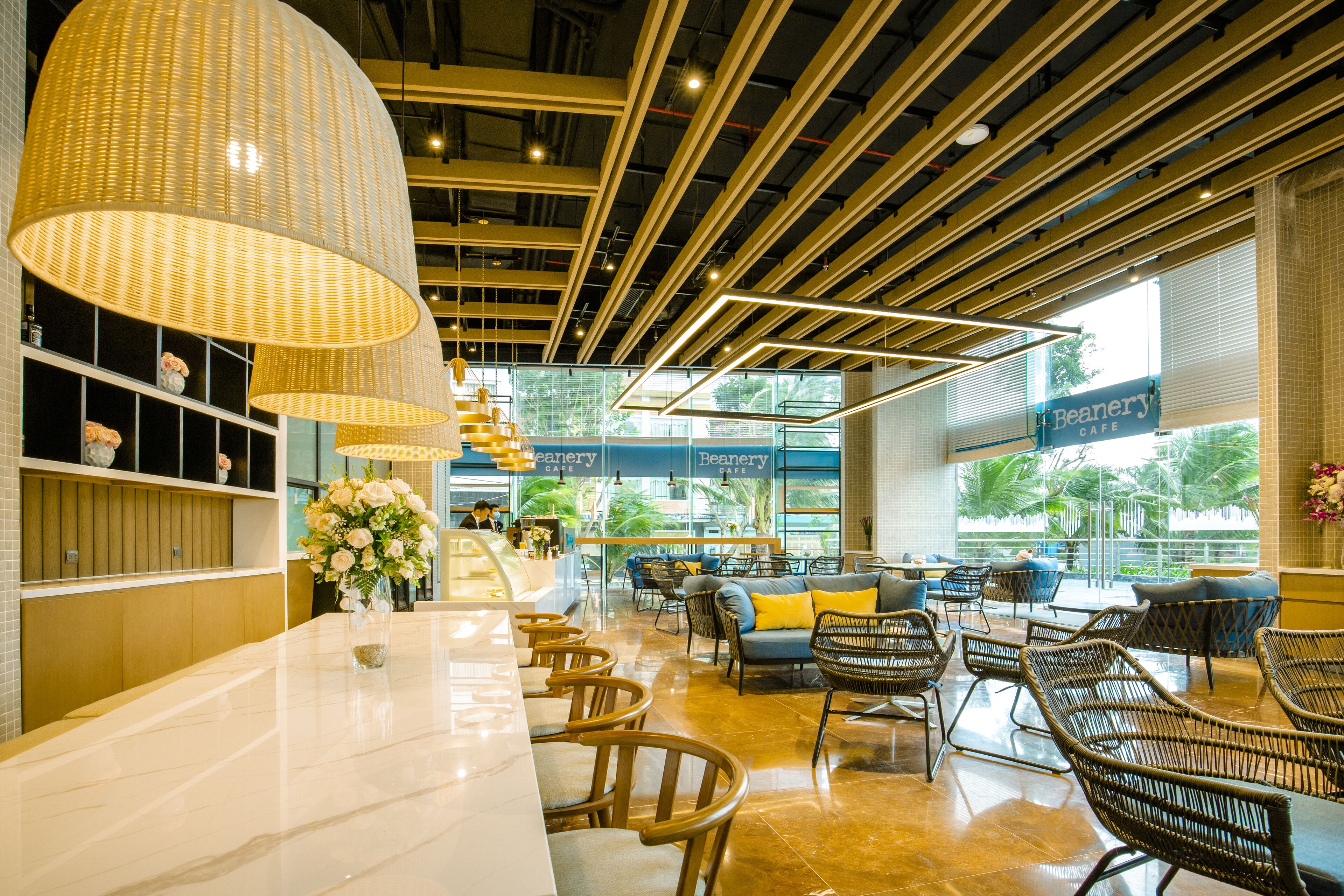 A modern cafe interior with a marble counter, wicker chairs, and large hanging lamps.