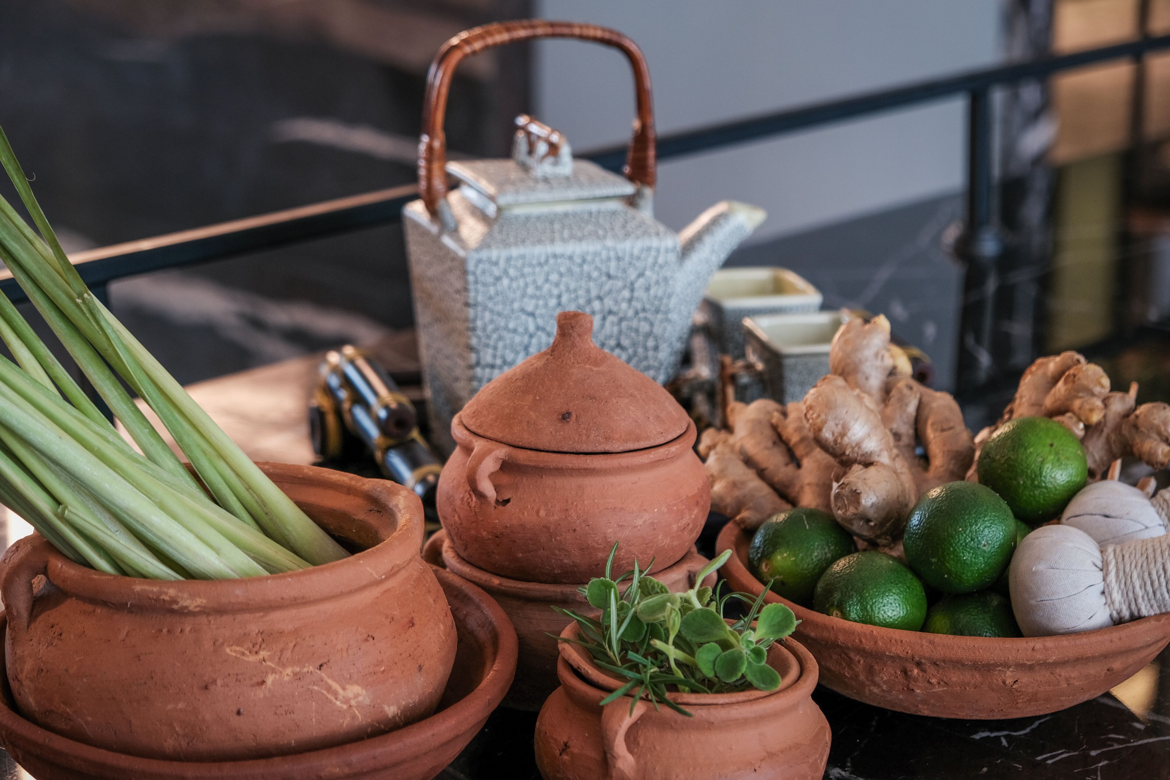 Terracotta pots with green onions, ginger, and limes on a table.