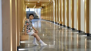 A person sitting on a bench in a corridor with a reflective floor and golden columns. - FLC City Hotel Beach Quy Nhon (Quy Nhon Nam)