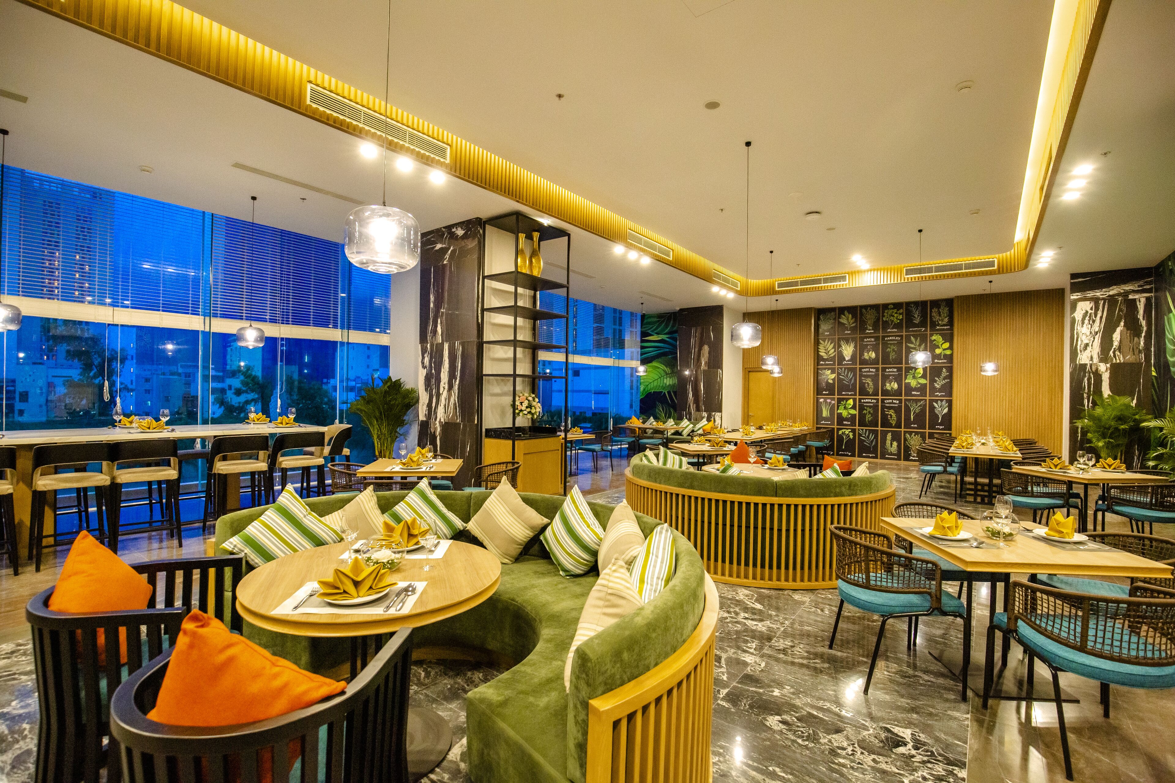 Ein modernes Restaurant mit runden Tischen, grünen Sofas und Blick auf die beleuchtete Stadt.