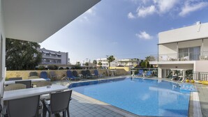 A swimming pool with lounge chairs and tables, surrounded by buildings and a clear sky. - Anemi Hotel (Hersonissos)